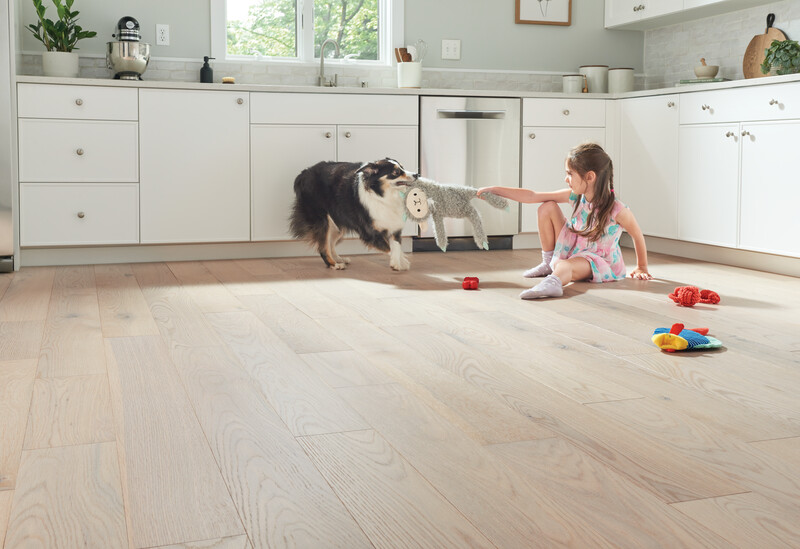 Little girl sitting on Dogwood Pro densified wood flooring in a kitchen playing with her dog